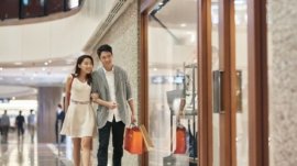 Full length of young couple window shopping in luxury mall. Male and female lovers admiring purse in store window. They are enjoying weekend together.