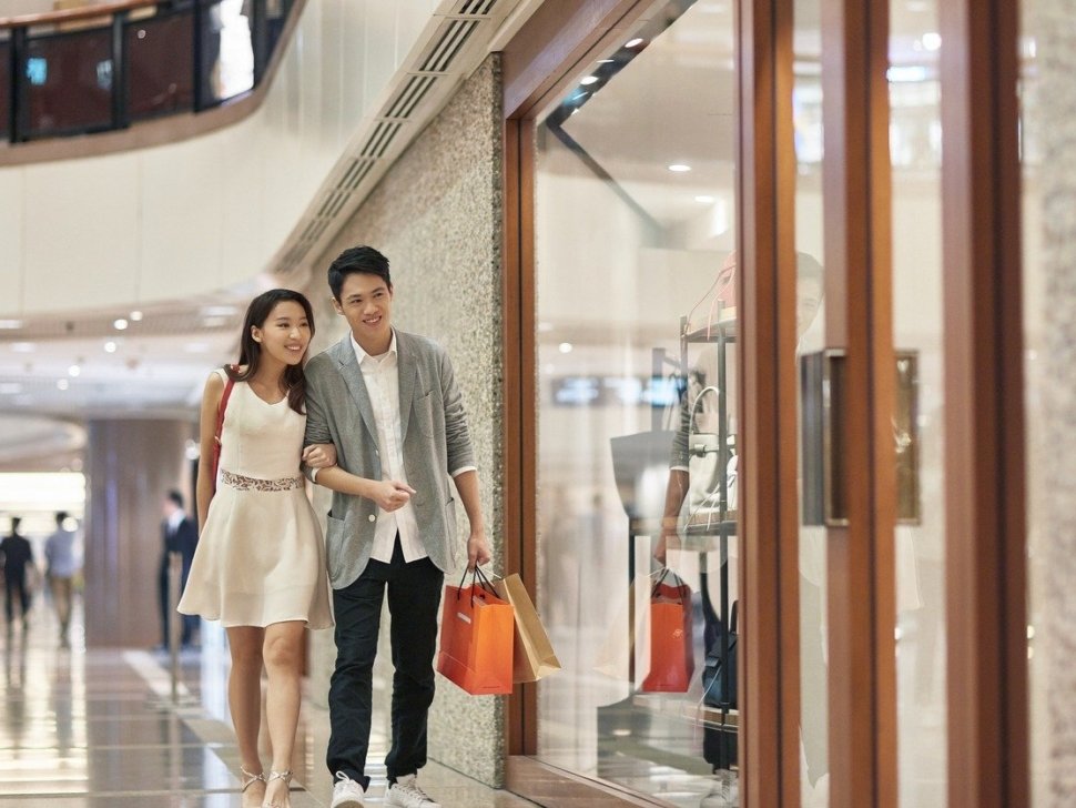 Full length of young couple window shopping in luxury mall. Male and female lovers admiring purse in store window. They are enjoying weekend together.