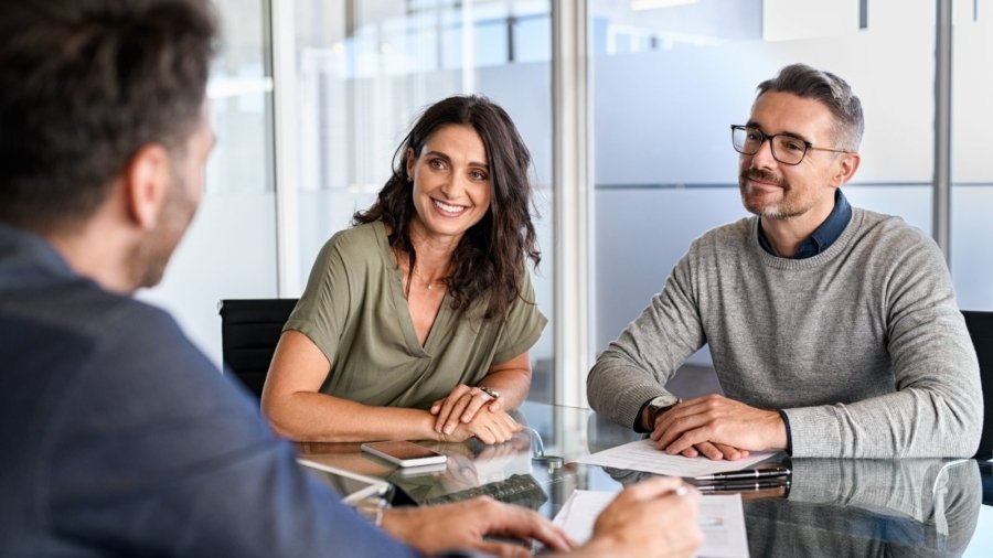 Smiling mature couple meeting with bank manager for investment. Beautiful mid adult woman with husband listening to businessman during meeting in conference room in modern office. Happy middle aged couple meeting loan advisor to buy a new home.